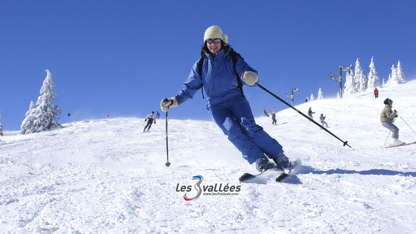 Skieuse en tenue bleue descend une piste enneigée aux Trois Vallées, entourée de sapins givrés - Hôtel Ski Alpes - Le Kaïla