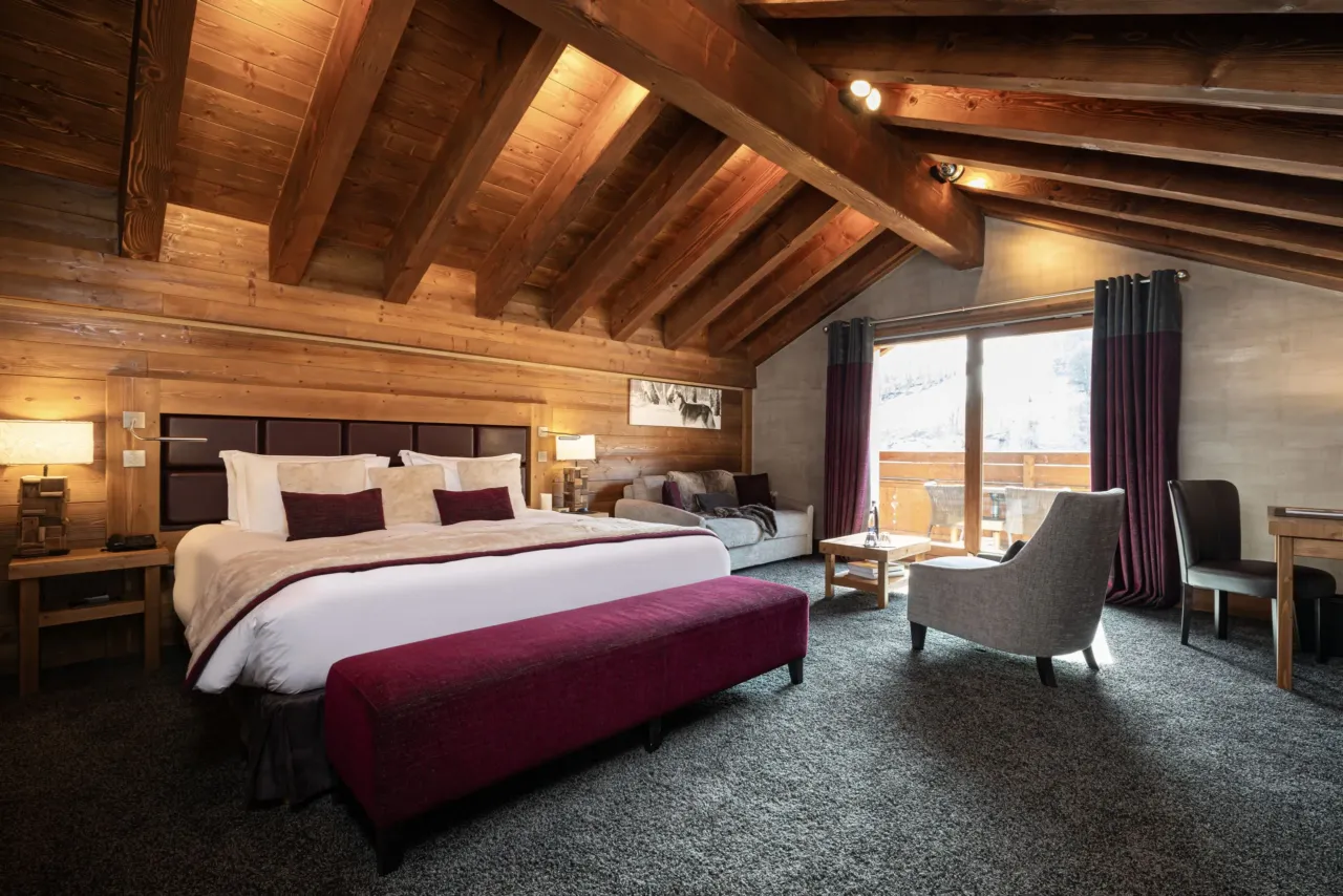 Suite chalet avec lit, salon avec poutres apparentes et balcon lumineux