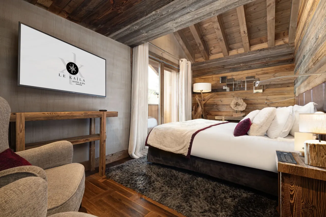Chambre élégante, mêlant bois rustique et confort moderne avec lit king-size, fauteuil douillet et écran TV - Week-end à Méribel - Le Kaïla