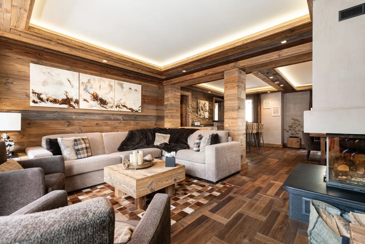 Salon de luxe dans un chalet de montagne avec murs en vieux bois, grand canapé d'angle, cheminée et décoration élégante - Hôtel Luxe Savoie - Le Kaïla